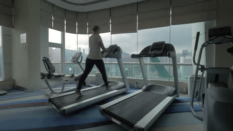 Clip-Einer-Frau-Auf-Dem-Laufband-Im-Fitnesscenter,-Die-Auf-Ein-Fenster-Mit-Stadtbild-Von-Hongkong,-China-Blickt