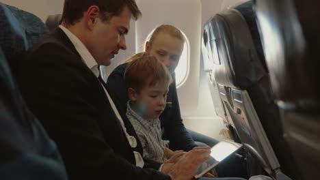 Dreiköpfige-Familie-Im-Flugzeug-Mit-Smartphone-Und-Tablet-PC