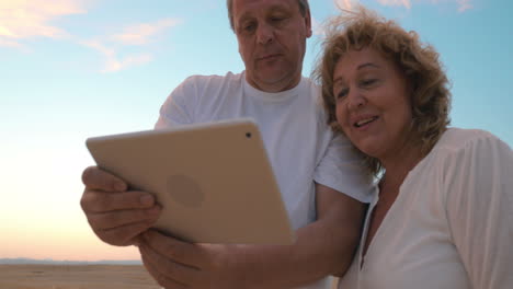 Älterer-Mann-Und-Frau-Mit-Tablet-Computer-Am-Strand