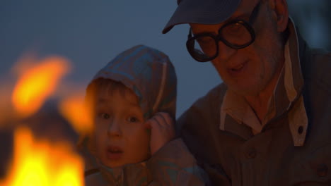 Elderly-man-sitting-with-small-boy-near-campfire