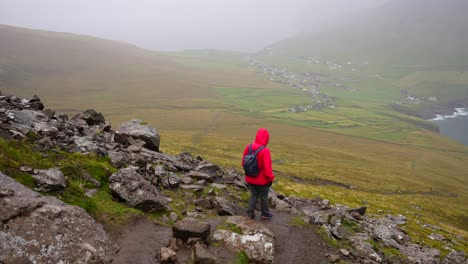 Woman-wearing-wet-red-jacket-hiking-down-Villingardalsfjall,-Faroe-Islands