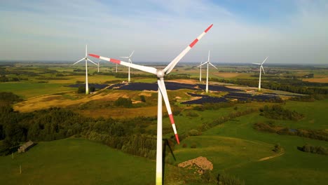 Aerial-footage-of-solar-panels-plant-and-wind-turbines-in-a-wind-farm-generating-green-electric-energy-on-a-wide-green-field-on-a-sunny-day,-in-Taurage,-Lithuania,-zooming-in,-4k