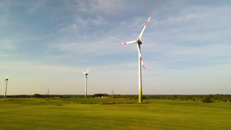 Drone-shot-of-the-wind-turbines-working-and-generating-green-electric-energy-on-a-wide-green-field-on-a-sunny-day,-use-of-renewable-resources-of-energy