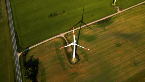 Drone-shot-of-the-wind-turbine-working-and-generating-green-electric-energy-on-a-green-field-on-a-sunny-day,-use-of-renewable-resources-of-energy,-top-down-shot