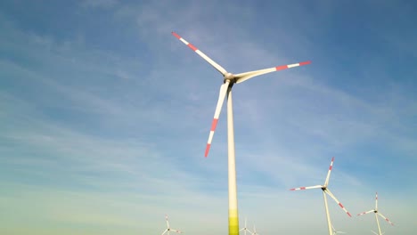 Low-angle-shot-of-wind-turbines-working-and-generating-green-electric-energy-in-a-wind-farm-under-blue-sky-on-a-sunny-day,-parallax
