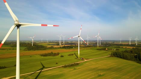 Drone-shot-of-the-wind-turbines-working-in-a-wind-farm-generating-green-electric-energy-on-a-wide-green-field-on-a-sunny-day,-use-of-renewable-resources-of-energy,-ascending