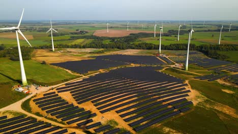 Aerial-footage-of-solar-panels-plant-and-wind-turbines-in-a-wind-farm-generating-green-electric-energy-on-a-wide-green-field-on-a-sunny-day,-in-Taurage,-Lithuania,-zooming-out