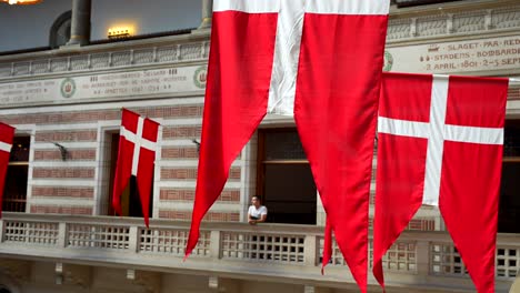 Danish-flags-handing-on-the-city-hall-of-Copenhagen,-man-admiring-from-balcony