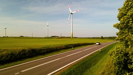 Car-driving-on-asphalt-road-in-a-wind-farm-with-wind-turbines-generating-green-electric-energy-in-the-background