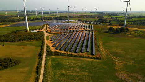 Aerial-footage-of-solar-panels-plant-and-wind-turbines-in-a-wind-farm-generating-green-electric-energy-on-a-wide-green-field-on-a-sunny-day,-in-Taurage,-Lithuania