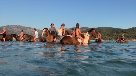 Group-of-tourists-have-fun-riding-horses-in-ocean-water-in-summer-season