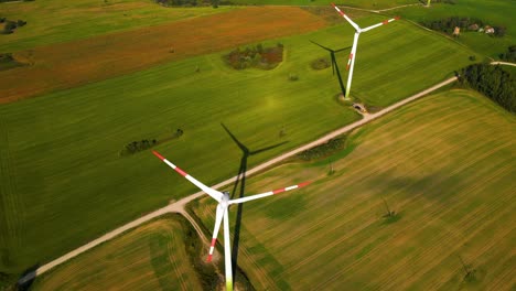 Drone-shot-of-the-wind-turbines-working-in-a-wind-farm-generating-green-electric-energy-on-a-wide-green-field-on-a-sunny-day,-in-the-background-there-is-solar-panels-plant