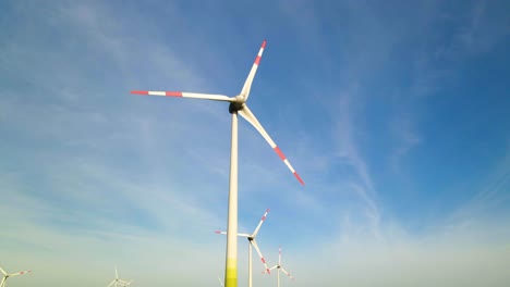Low-angle-shot-of-wind-turbines-working-and-generating-green-electric-energy-in-a-wind-farm-under-blue-sky-on-a-sunny-day,-still-shot