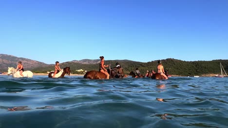 Group-of-people-have-fun-riding-horse-in-ocean-water-in-summer-season