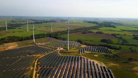 Aerial-footage-of-solar-panels-plant-and-wind-turbines-in-a-wind-farm-generating-green-electric-energy-on-a-wide-green-field-on-a-sunny-day,-in-Taurage,-Lithuania,-zooming-in