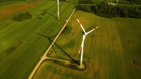 Drohnenaufnahme-Einiger-Windturbinen,-Die-An-Einem-Sonnigen-Tag-Auf-Einer-Grünen-Wiese-Arbeiten-Und-Grüne-Elektrische-Energie-Erzeugen,-Nutzung-Erneuerbarer-Energiequellen,-Aufnahme-Von-Oben-Nach-Unten