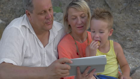 Motherfather-and-son-watching-video-on-pad-while-sitting-on-beach