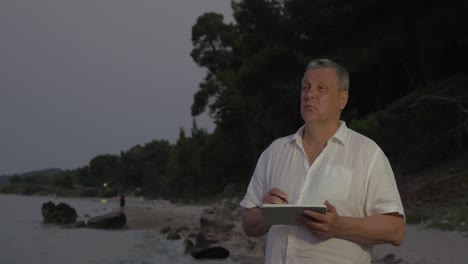 Senior-man-using-tablet-PC-on-beach-in-late-evening