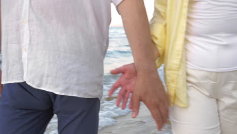 Senior-couple-holding-hands-during-walk-on-beach