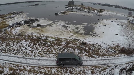Flying-over-car-driving-by-the-waterside-in-winter