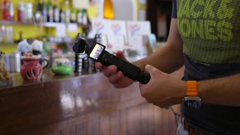 Content-Creator-Attaching-Battery-Handle-And-Mini-Tripod-Beside-Cafe-Bar