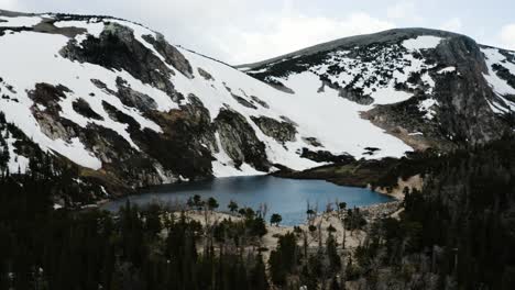 Drone-shot-pushing-towards-the-isolated-Saint-Mary's-Lake-lying-beneath-a-semi-permanent-snowfield-in-Colorado