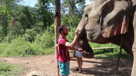Young-man-at-Sanctuary-smiling-happy-while-hand-feeding-and-petting-elephant
