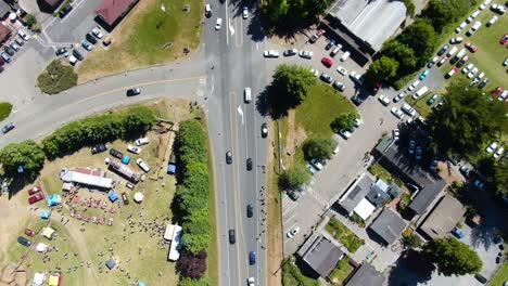 Drone-top-view-video-showcasing-a-highway-intersecting-with-a-road,-surrounded-by-numerous-parked-cars-in-a-rural-area-with-green-trees,-in-Bodega-Bay,-Gualala-Coast,-California
