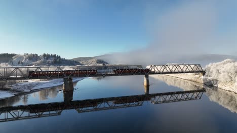 Aerial-shot-of-a-misty-sunny-layered-Norwegian-landscape-with-a-train-bridge
