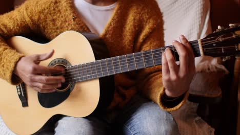 Attractive-man-with-long-dreadlocks-plays-the-guitar-in-a-cozy-living-room