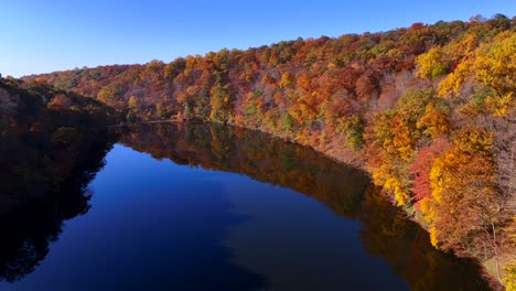 An-aerial-view-of-a-reflective-lake-on-a-sunny-day-with-colorful-autumn-trees-on-both-sides