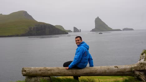 Handsome-man-contemplates-Faroe-Islands-looking-at-Drangarnir-and-Tindholmur-and-smiling-to-the-camera