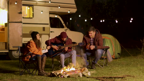 Man-singing-a-song-on-guitar-for-his-friends-around-camp-fire