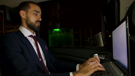 Businessman-in-suit-sitting-on-the-back-seat-of-his-limousine-working-on-laptop