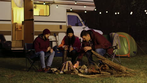 Man-helping-friend-to-light-the-camp-fire-in-front-of-retro-camper