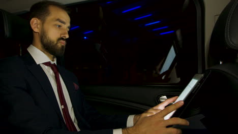 Businessman-working-on-his-laptop-on-the-backseat-of-his-luxury-car-with-personal-driver