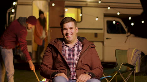 Happy-young-man-sitting-on-camping-chair-looking-at-the-camera