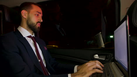 Businessman-in-suit-working-late-on-his-laptop-on-the-back-seat-of-his-car