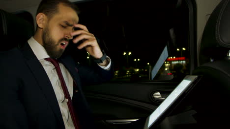 Yawning-businessman-in-suit-checking-his-watch-at-night-in-the-back-seat-of-his-limousine.
