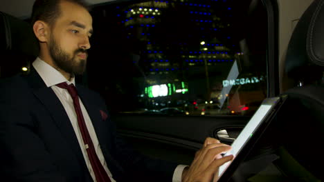 CEO-in-business-suit-working-on-tablet-in-the-back-of-luxury-car
