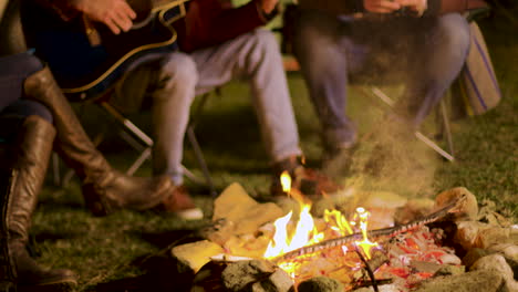 Camping-fire-burning-while-man's-singing-on-guitar