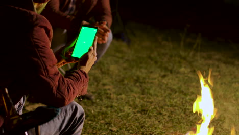 Man-looking-at-this-phone-with-green-screen-around-camp-fire