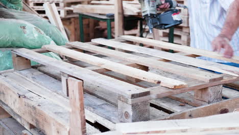 Arbeiter-In-Einer-Holzfabrik,-Der-Mit-Einem-Nagelgewehr-Eine-Holzpalette-Herstellt