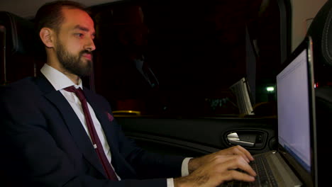Bearded-businessman-typing-on-laptop-in-the-backseat-of-his-limousine
