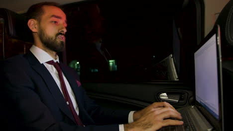 Focused-businessman-in-the-back-seat-of-limousine-typing-on-laptop-at-night