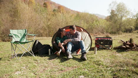 Beautiful-young-couple-having-a-conversation-in-front-of-their-camping-tent