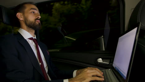 Businessman-in-suit-looking-over-the-window-of-his-limousine-and-typing-on