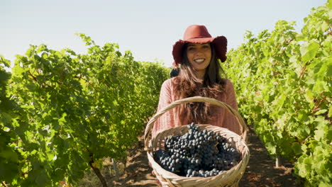 Smiling-woman-lifting-a-basket-with-grapes