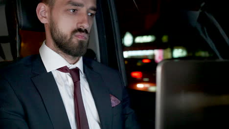 Successful-bearded-businessman-working-on-laptop-from-the-back-sea-of-his-limousine