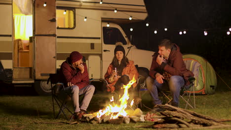Group-of-friends-gathered-around-camp-fire-in-a-cold-night-of-autumn